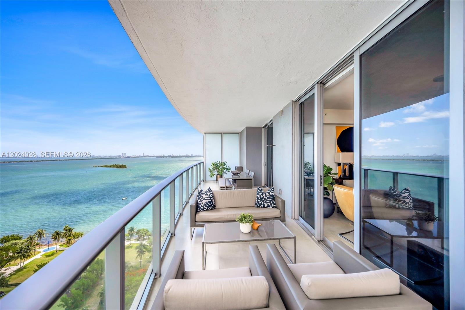 A balcony with outdoor seating overlooks a large body of water and a park — 488 NE 18th St # 2011, Miami FL 33132, MIAMI, FL
