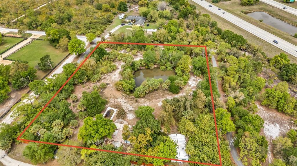 An aerial view shows a wooded lot with a central pond and two small structures — 24789 NOVA LANE, PUNTA GORDA, FL