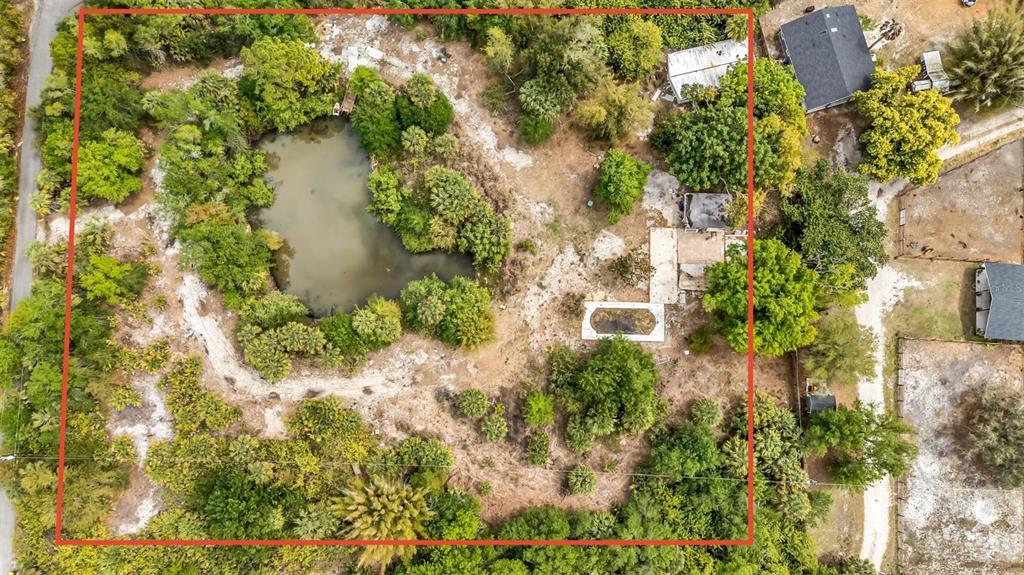 An aerial view shows a large, wooded lot containing a pond, a pool, and structures — 24789 NOVA LANE, PUNTA GORDA, FL