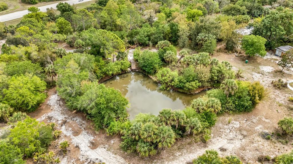 An aerial view shows a small pond surrounded by dense trees and vegetation — 24789 NOVA LANE, PUNTA GORDA, FL