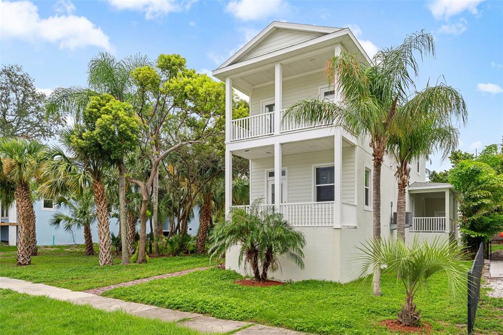 A two-story light green house with double-stacked porches stands among palm trees and grass — 385 GEORGIA AVENUE, CRYSTAL BEACH, FL