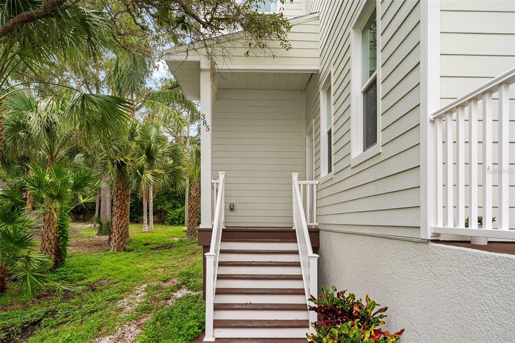 Exterior view of a house entrance with wooden stairs, white railings, and light-colored siding — 385 GEORGIA AVENUE, CRYSTAL BEACH, FL