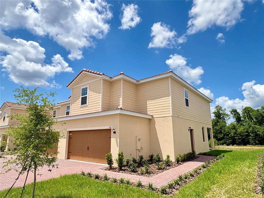 A two-story tan house with a brown garage door and a brick paver driveway — 568 BAY LEAF DRIVE, POINCIANA, FL