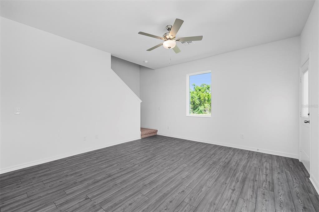An empty room with gray wood-look flooring, white walls, a ceiling fan, and stairs — 568 BAY LEAF DRIVE, POINCIANA, FL