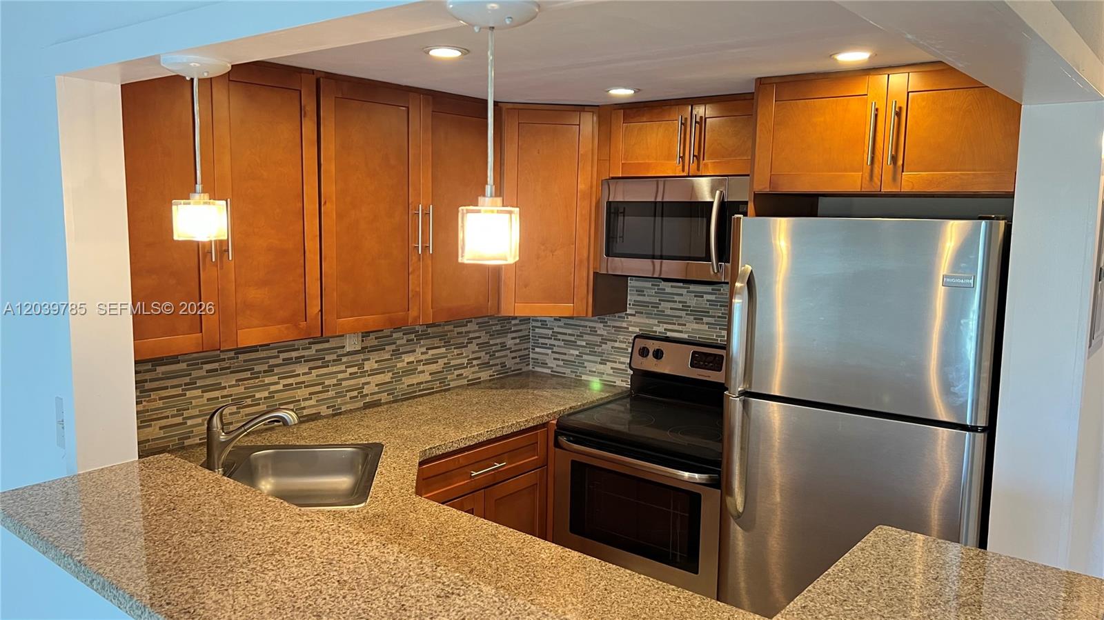 A kitchen features wood cabinets, granite countertops, stainless steel appliances, and a tiled backsplash — 4550 NW 9th St # 516E, Miami FL 33126, MIAMI, FL