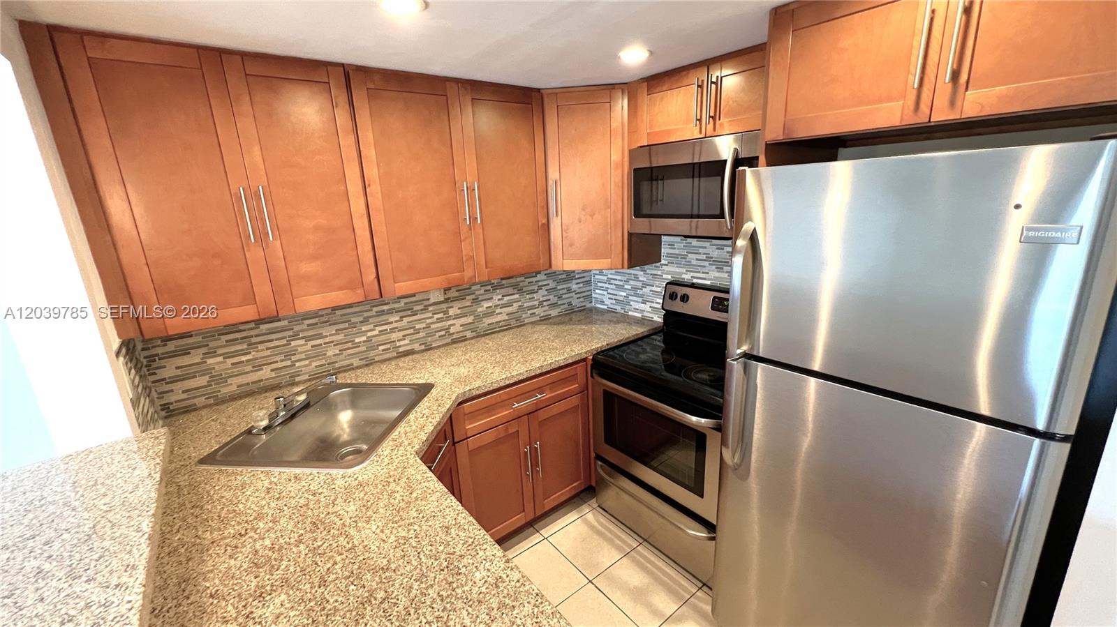 A kitchen features wood cabinets, granite countertops, stainless steel appliances, and a tiled backsplash — 4550 NW 9th St # 516E, Miami FL 33126, MIAMI, FL