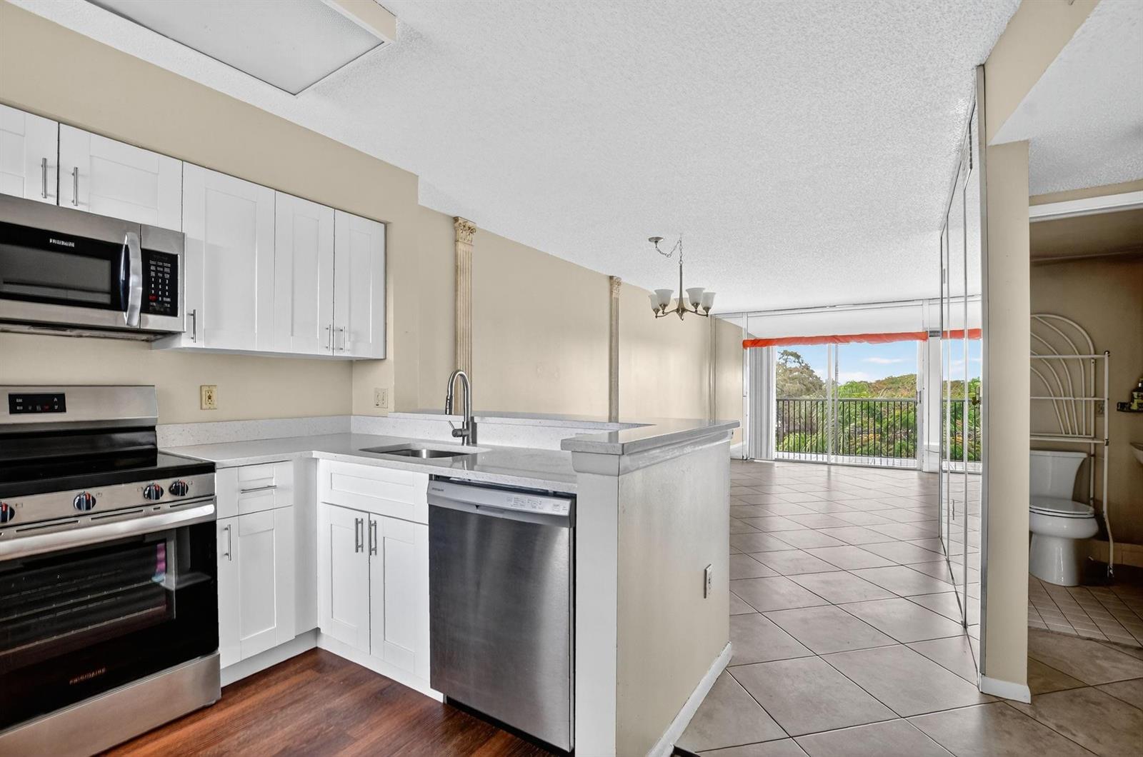 A kitchen with white cabinets and stainless steel appliances overlooks a living area and balcony — 2236 N Cypress Bend Drive # 508, Pompano Beach FL 33069, POMPANO BEACH, FL