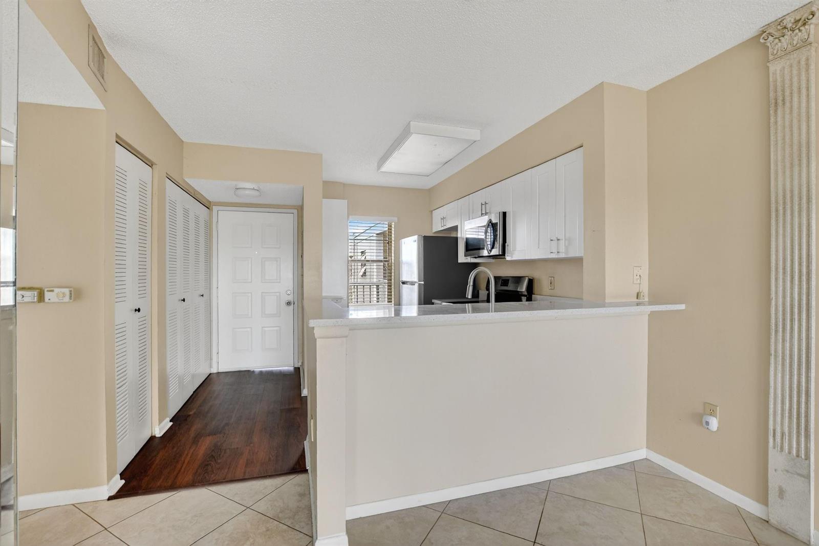 A kitchen with white cabinets, stainless steel appliances, and a breakfast bar overlooks a hallway — 2236 N Cypress Bend Drive # 508, Pompano Beach FL 33069, POMPANO BEACH, FL