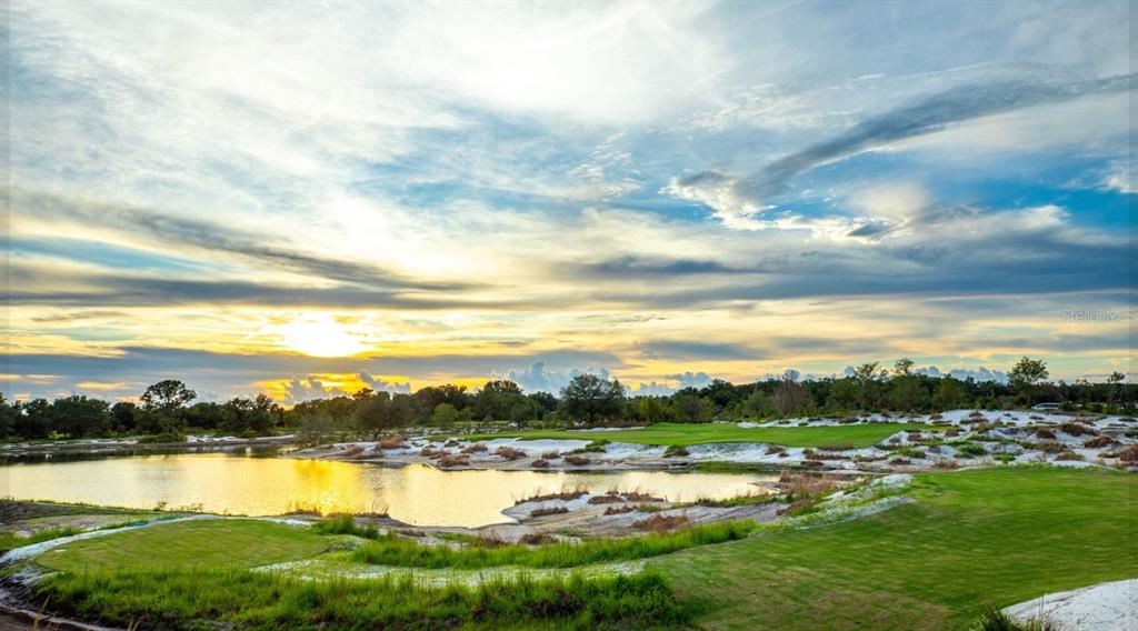 A golf course hole features a large water hazard, sand bunkers, and green grass at sunset — 33712 BELLINO PLACE, MYAKKA CITY, FL