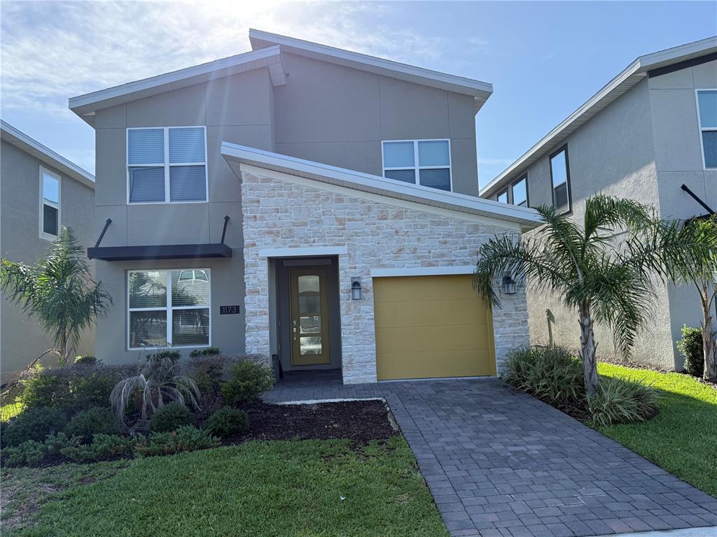 A two-story house features a stone facade, a yellow garage door, and a paved driveway — 1173 KINGSBARN STREET, DAVENPORT, FL