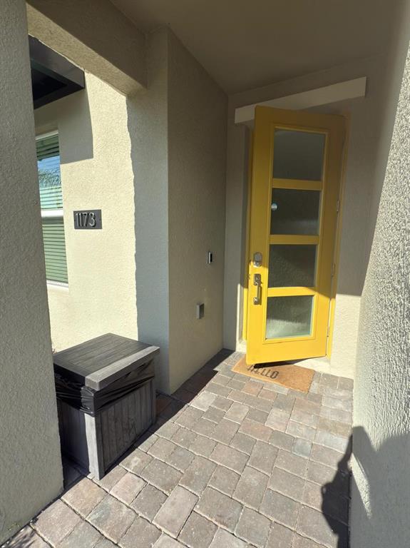 A yellow front door with glass panels opens onto a paved entryway with a package box — 1173 KINGSBARN STREET, DAVENPORT, FL