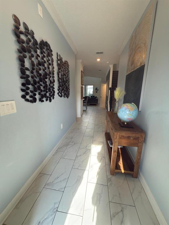 A hallway with light blue walls, marble-look tile flooring, wall art, and a wooden console table — 1173 KINGSBARN STREET, DAVENPORT, FL