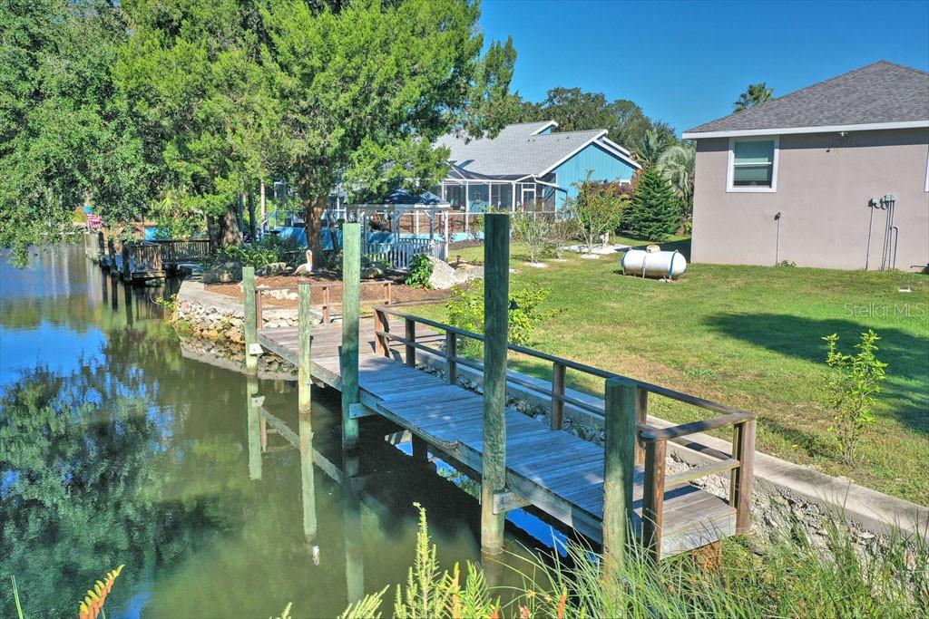 A wooden dock extends into a canal next to a grassy yard and houses — 11752 W VALLEY SPRING LANE, HOMOSASSA, FL