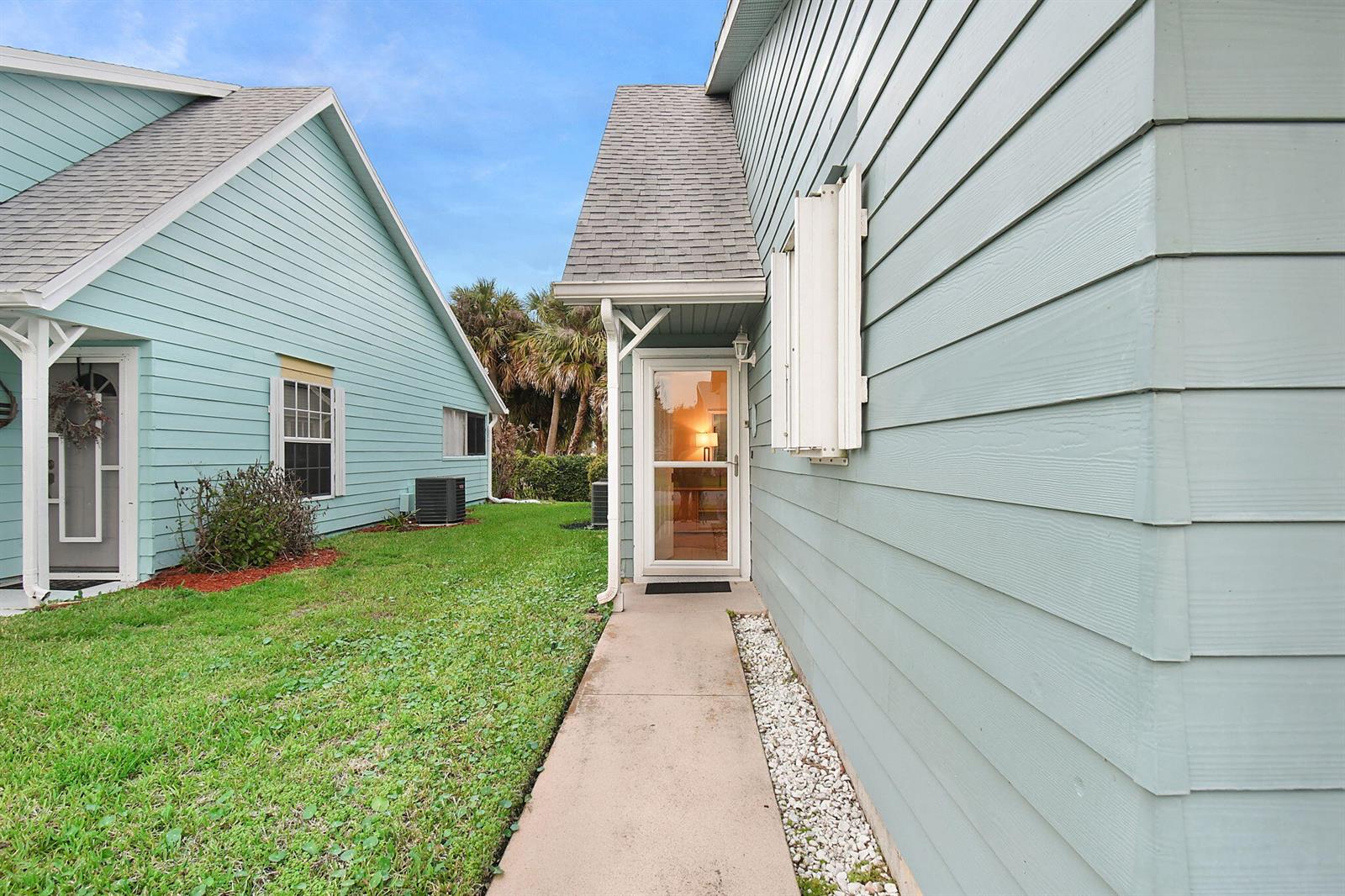 A concrete walkway leads to the glass-paned front door of a light blue house — 4072 Gator Trace Road, Fort Pierce FL 34982, FORT PIERCE, FL