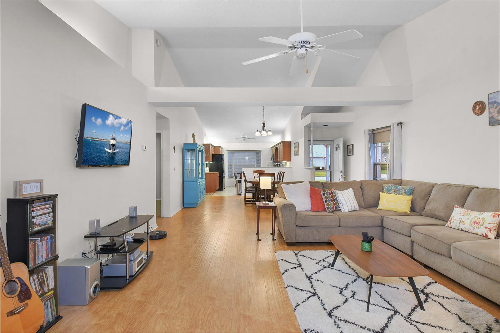 A living room with vaulted ceilings, wood-look flooring, and an open layout leading to a kitchen — 4072 Gator Trace Road, Fort Pierce FL 34982, FORT PIERCE, FL