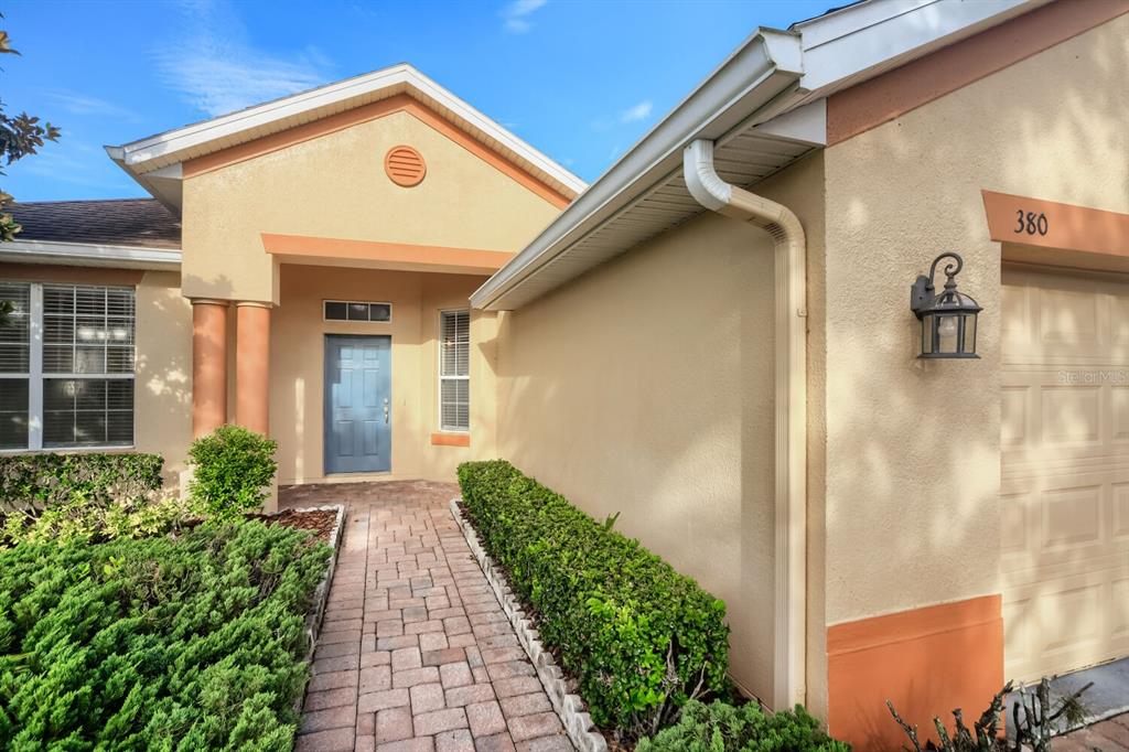 A paved walkway leads to the front entrance of a house with a tan exterior — 380 SORRENTO ROAD, KISSIMMEE, FL