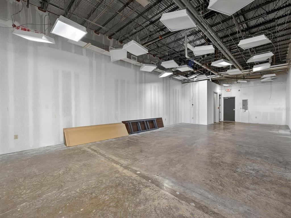 An unfinished commercial space features exposed ceiling beams, hanging light fixtures, and concrete flooring — 250 AVENUE K SW UNIT 104, WINTER HAVEN, FL