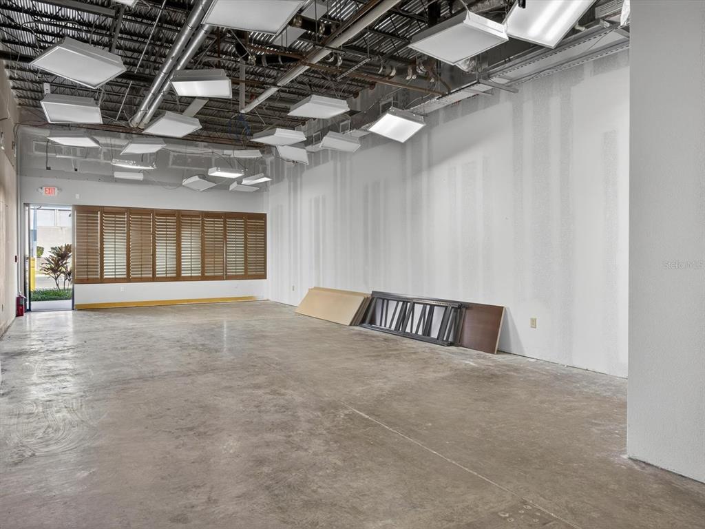 An empty commercial space features a concrete floor, exposed ceiling, and wood-shuttered windows — 250 AVENUE K SW UNIT 104, WINTER HAVEN, FL