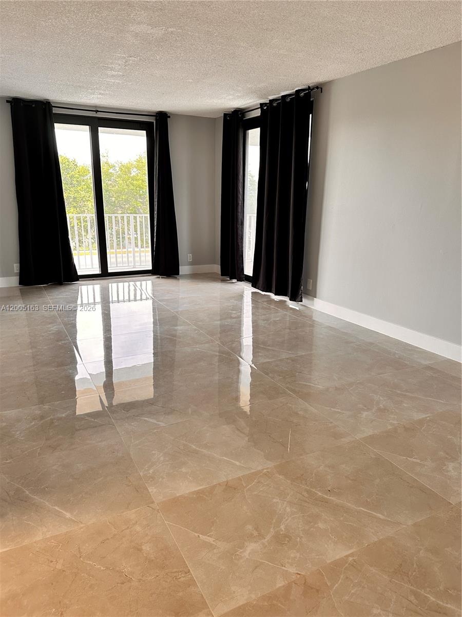 An empty room features large beige floor tiles, grey walls, and black curtains over sliding doors — 901 Hillcrest Dr # 315, Hollywood FL 33021, HOLLYWOOD, FL