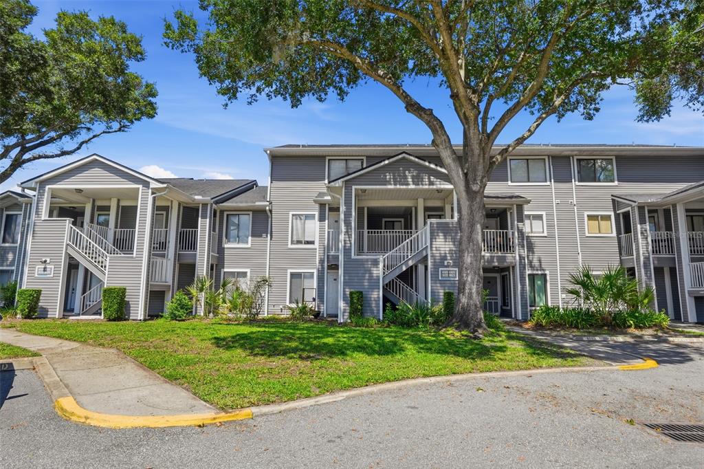 A three-story apartment building with gray siding, white railings, and a large tree in front — 2216 STONINGTON AVENUE UNIT 2216, ORLANDO, FL