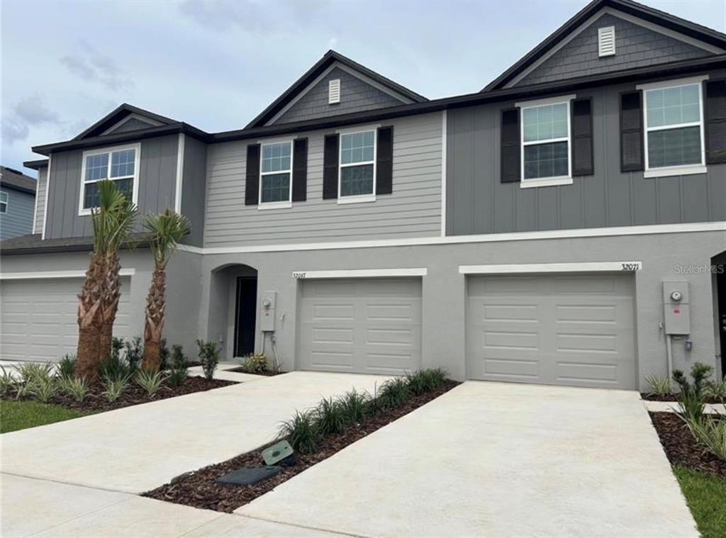 A two-story townhouse exterior features gray siding, multiple garage doors, and a concrete driveway — 32079 EASTERN REDBUD BRANCH, SAN ANTONIO, FL