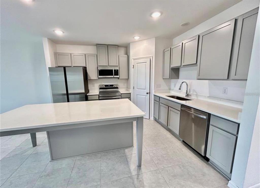 A modern kitchen features gray cabinets, stainless steel appliances, a white island, and tile flooring — 32079 EASTERN REDBUD BRANCH, SAN ANTONIO, FL