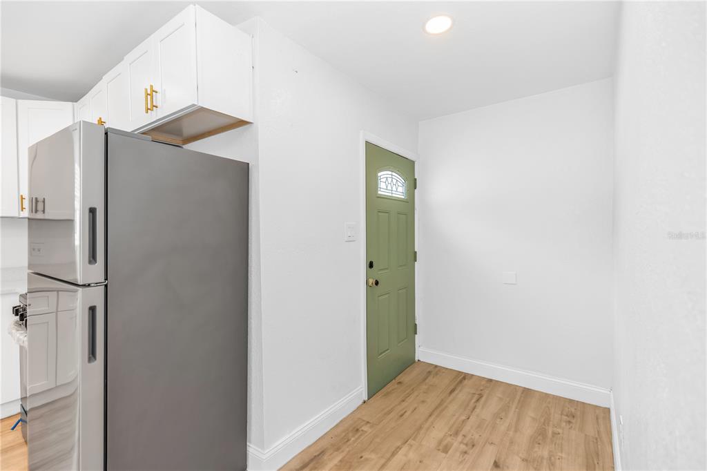 A kitchen area features a stainless steel refrigerator, white cabinets, and a green exterior door — 1262 SEMINOLA BOULEVARD, CASSELBERRY, FL