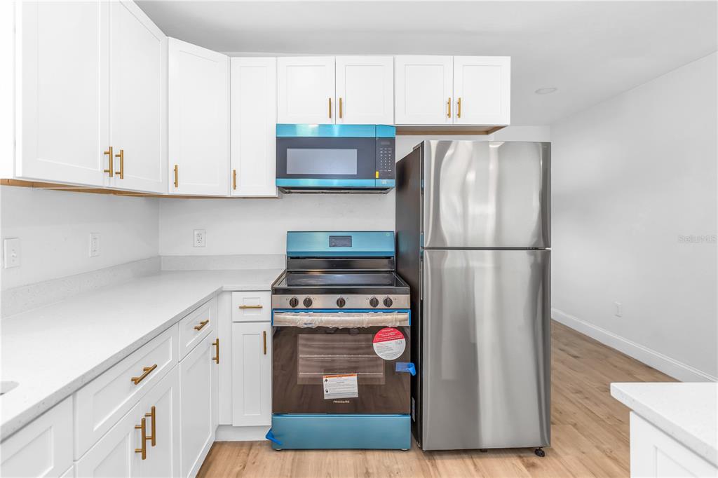 A kitchen features white cabinets, stainless steel appliances, and light wood-look flooring — 1262 SEMINOLA BOULEVARD, CASSELBERRY, FL