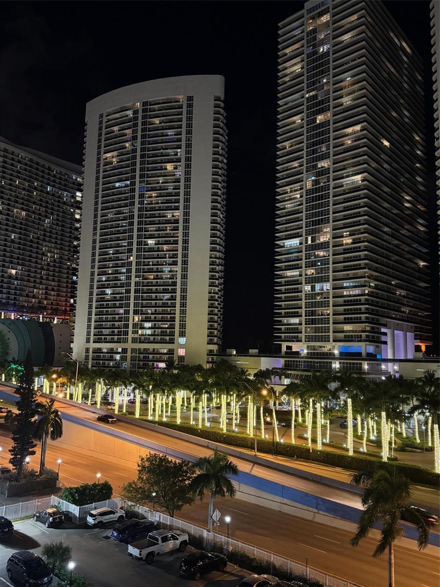 A night view of two tall residential towers overlooking a highway lined with illuminated palm trees — 1849 S Ocean Drive # 711, Hallandale Beach FL 33009, HALLANDALE BEACH, FL