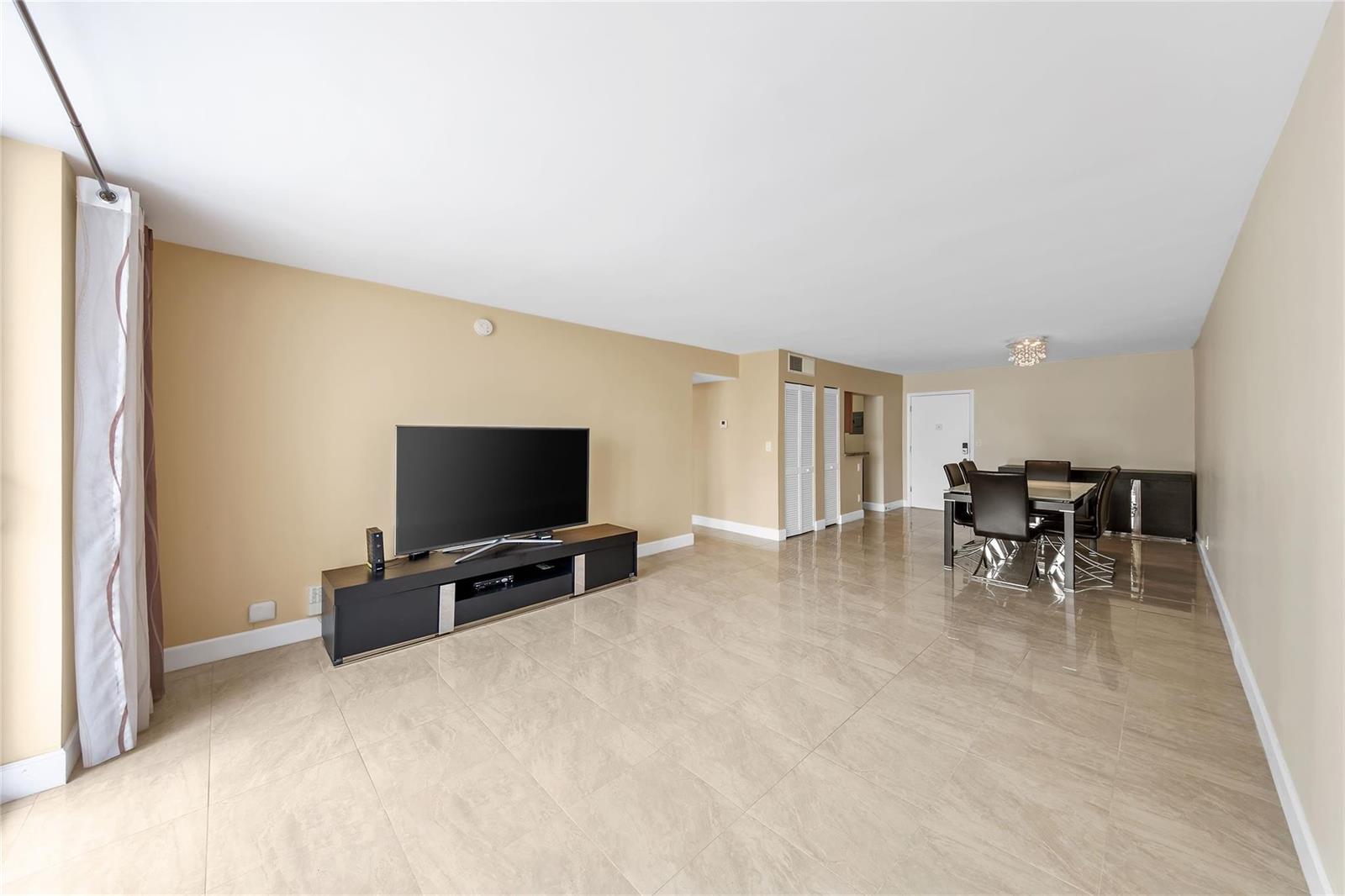 A living and dining area with beige walls, tile flooring, and a black media console — 1849 S Ocean Drive # 711, Hallandale Beach FL 33009, HALLANDALE BEACH, FL