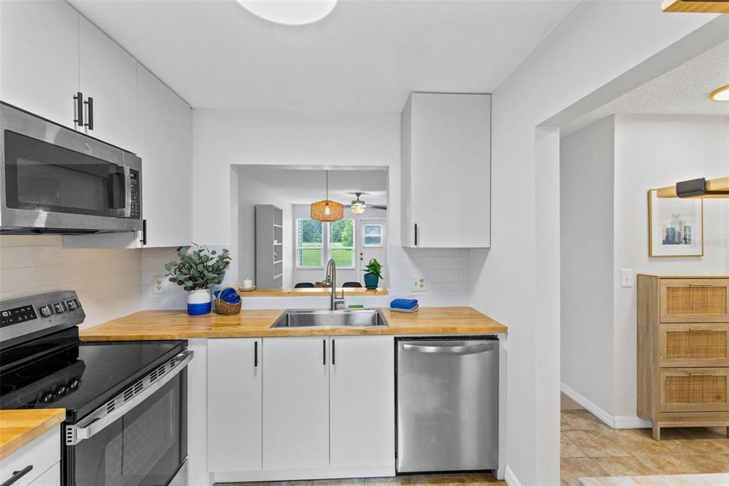 A kitchen features white cabinets, a wood countertop, stainless steel appliances, and a pass-through window — 9514 DARIEN AVENUE UNIT 9514, ORLANDO, FL