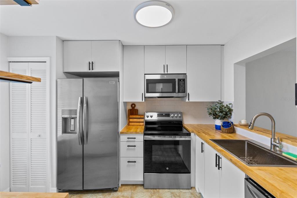 A kitchen features white cabinets, stainless steel appliances, and wood countertops — 9514 DARIEN AVENUE UNIT 9514, ORLANDO, FL