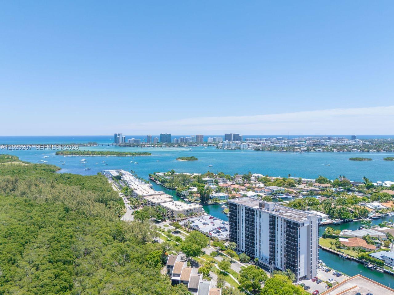 An aerial view shows a coastal neighborhood with a high-rise building, canals, and ocean — 2500 NE 135th St # B508, North Miami FL 33181, NORTH MIAMI, FL