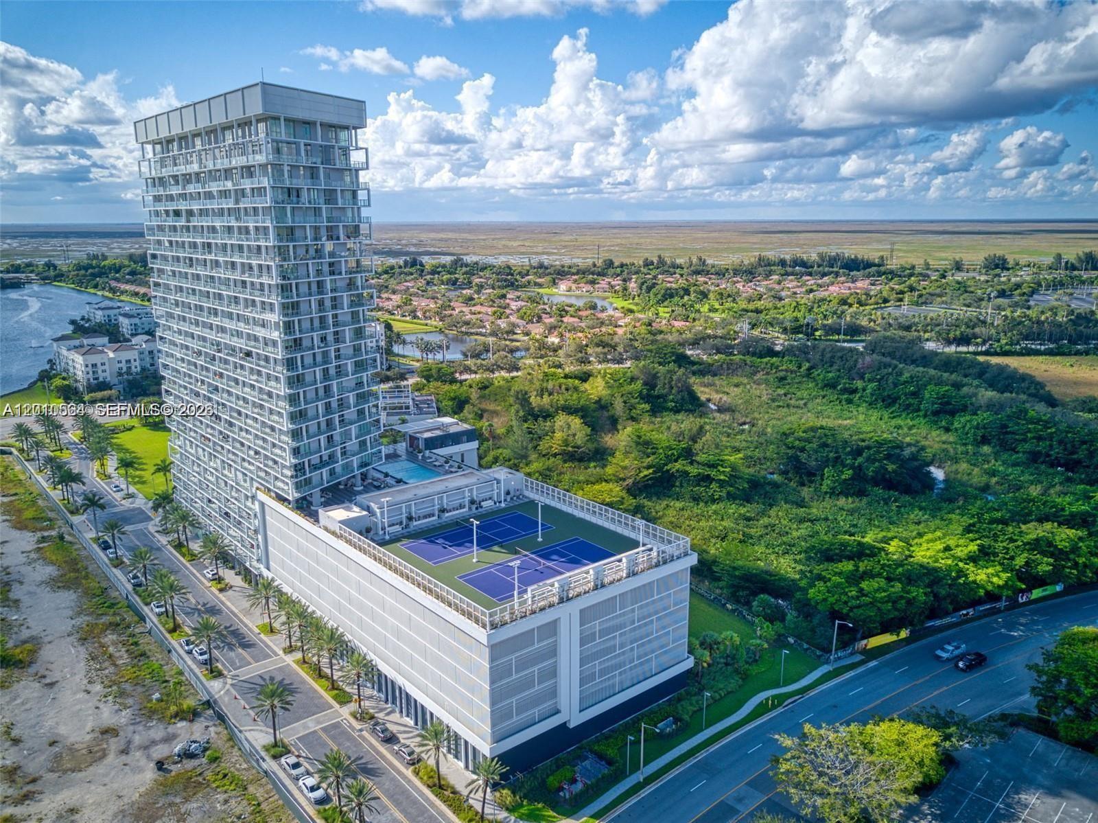 An aerial view shows a tall residential tower with a rooftop tennis court and pool — 2000 Metropica Way # 2304, Sunrise FL 33323, SUNRISE, FL