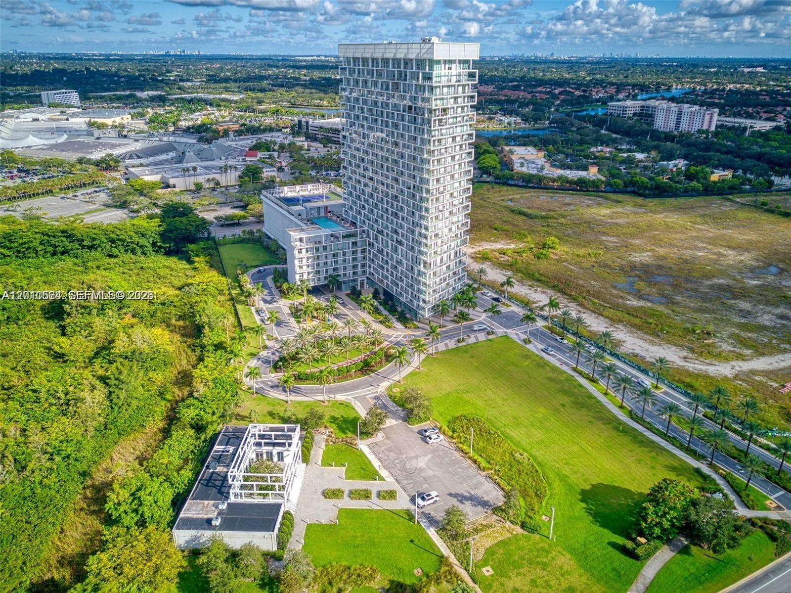 An aerial view shows a tall residential tower surrounded by green lawns and parking areas — 2000 Metropica Way # 2304, Sunrise FL 33323, SUNRISE, FL