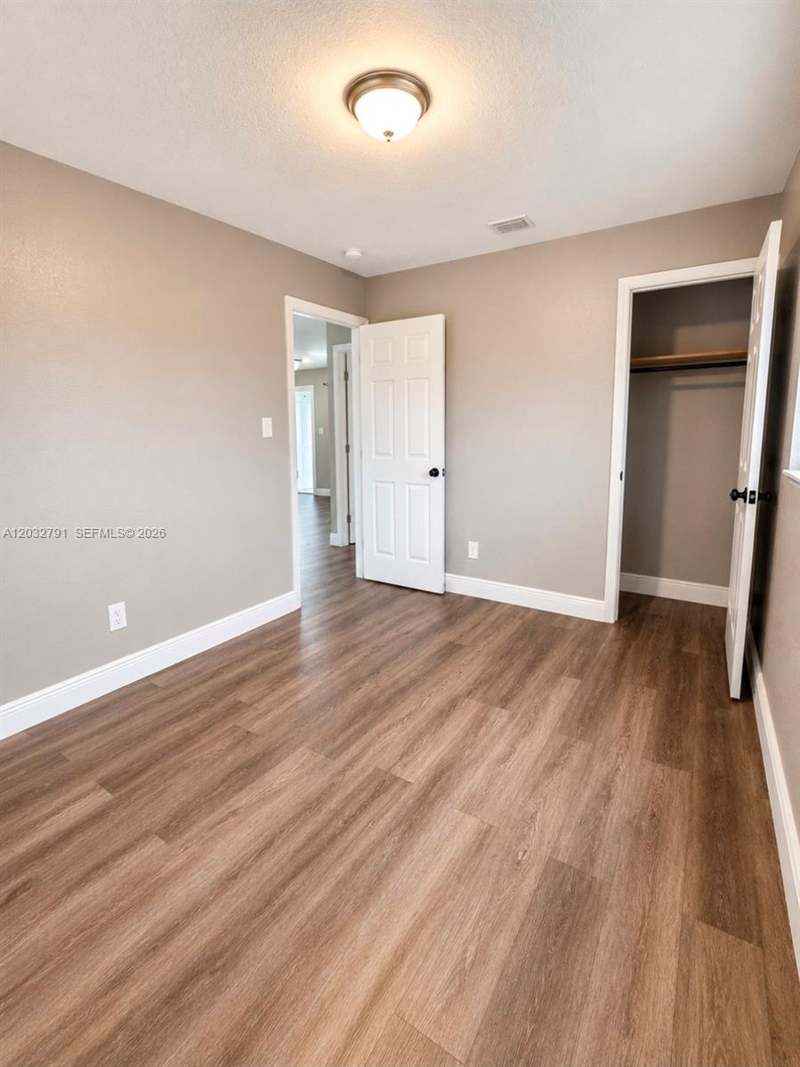 An empty bedroom features light-colored walls, wood-look flooring, a closet, and a white door — 2350 NW 12th Ct # 0, Pompano Beach FL 33069, POMPANO BEACH, FL