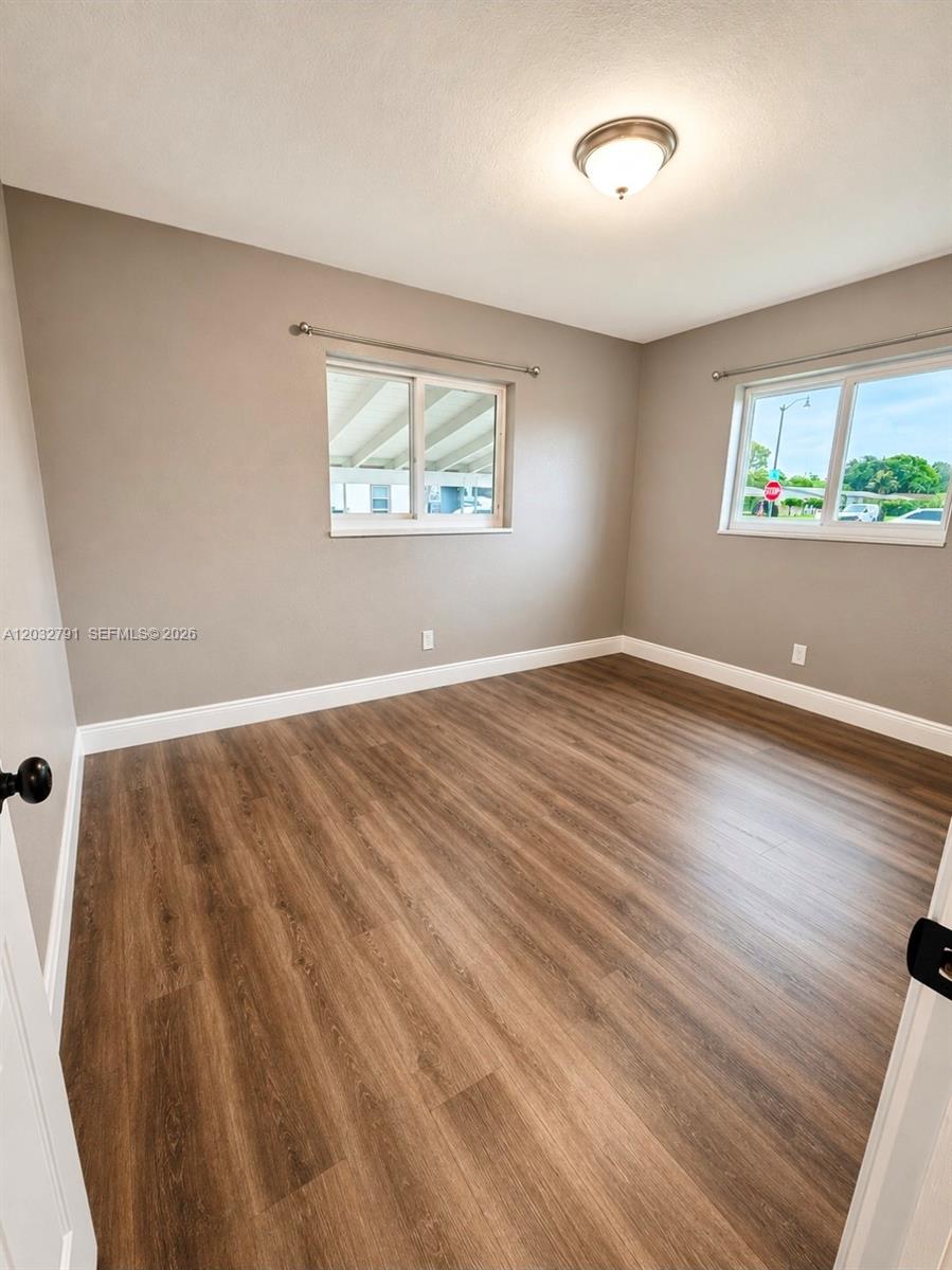 An empty bedroom features light gray walls, wood-look flooring, and two windows with curtain rods — 2350 NW 12th Ct # 0, Pompano Beach FL 33069, POMPANO BEACH, FL