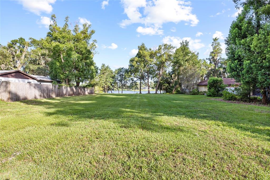 A large, grassy vacant lot features a wooden fence and a view of a lake — 18703.5 LAKESHORE DR, LUTZ, FL