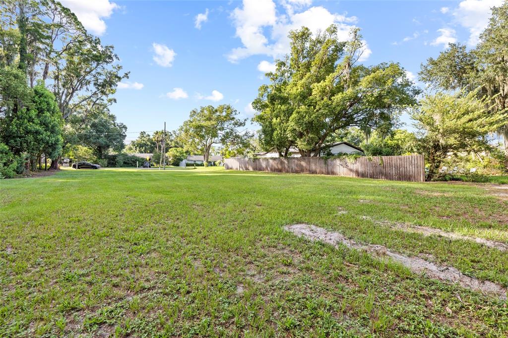 A grassy, vacant lot features a wooden fence and mature trees under a blue sky — 18703.5 LAKESHORE DR, LUTZ, FL