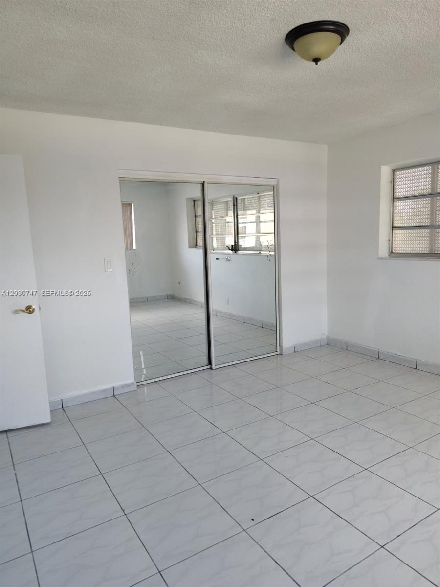 A room with white walls, light-colored tiled flooring, and sliding mirrored closet doors — 200 NE 12th Ave # 1C, Hallandale Beach FL 33009, HALLANDALE BEACH, FL
