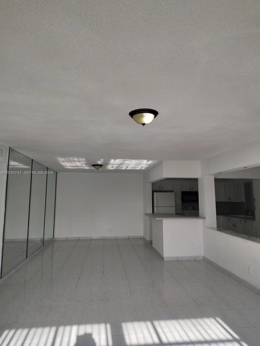 An open living area features white tile floors, mirrored closet doors, and a kitchen pass-through — 200 NE 12th Ave # 1C, Hallandale Beach FL 33009, HALLANDALE BEACH, FL