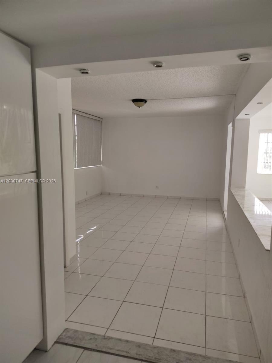 An empty room features white tile flooring, a textured ceiling, and recessed lighting — 200 NE 12th Ave # 1C, Hallandale Beach FL 33009, HALLANDALE BEACH, FL