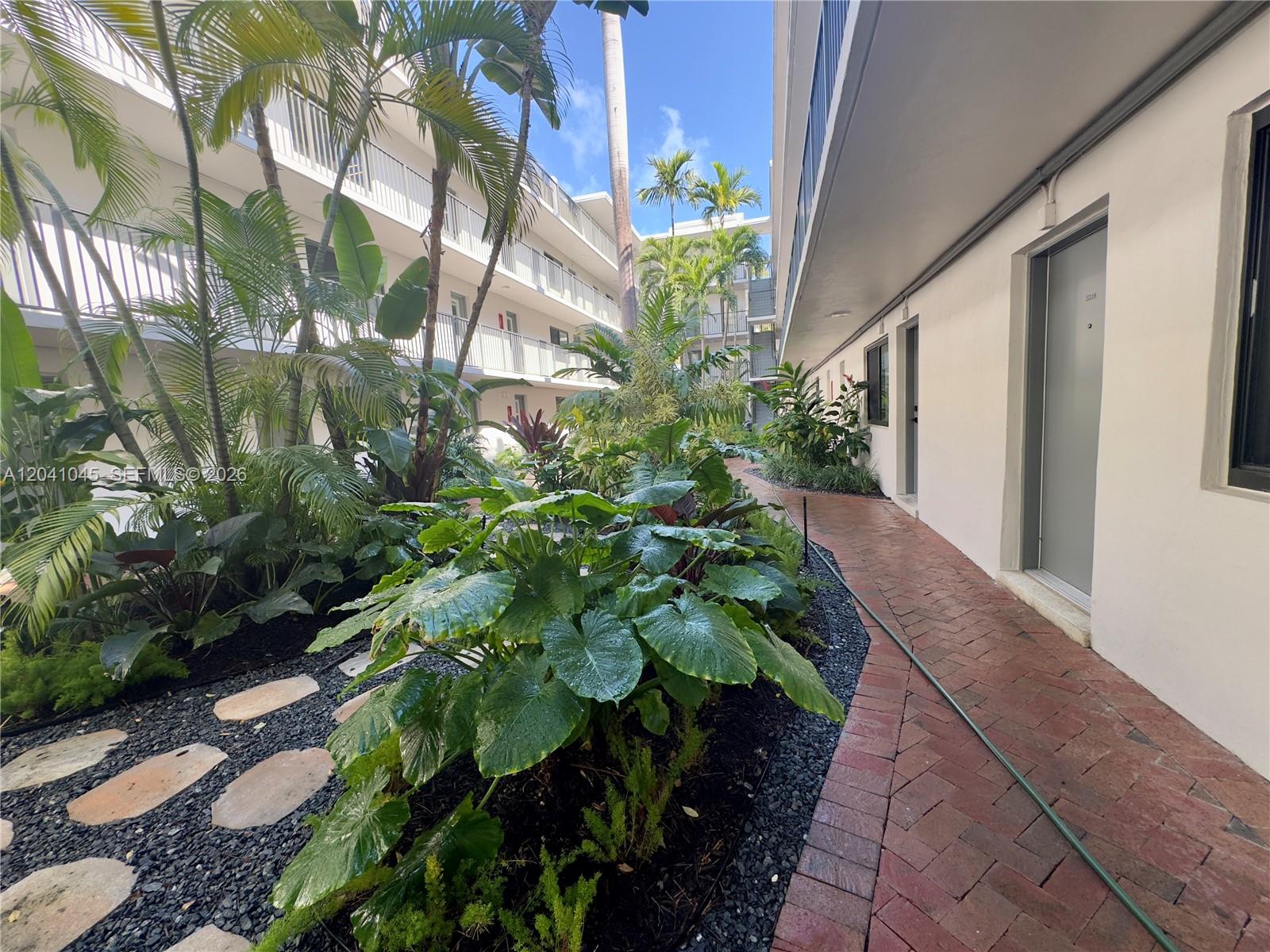 A brick walkway leads through a landscaped courtyard between two levels of apartment balconies — 3242 Mary St # S115, Miami FL 33133, MIAMI, FL