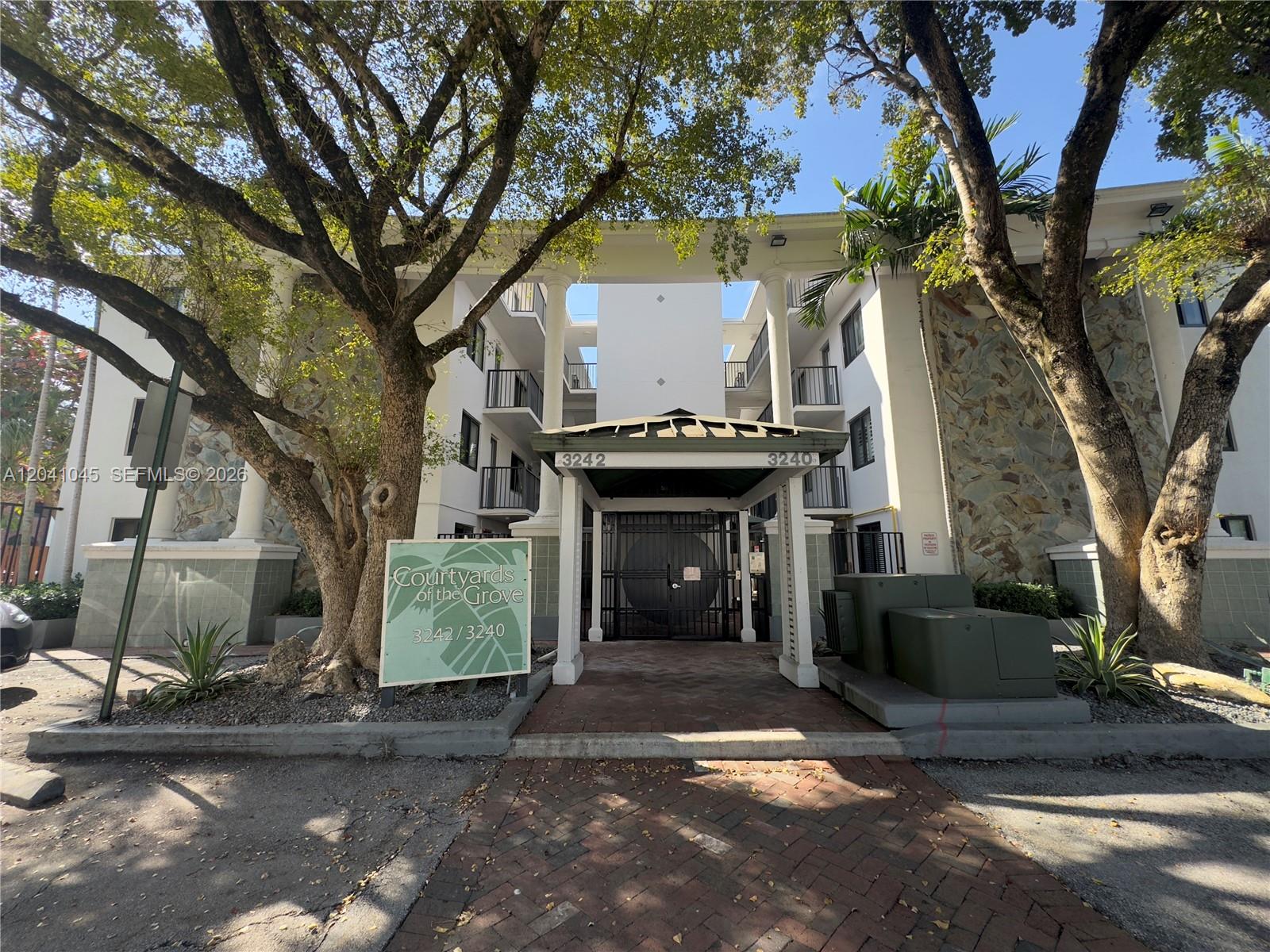 The exterior of a multi-story apartment building features a covered entrance and a prominent sign — 3242 Mary St # S115, Miami FL 33133, MIAMI, FL