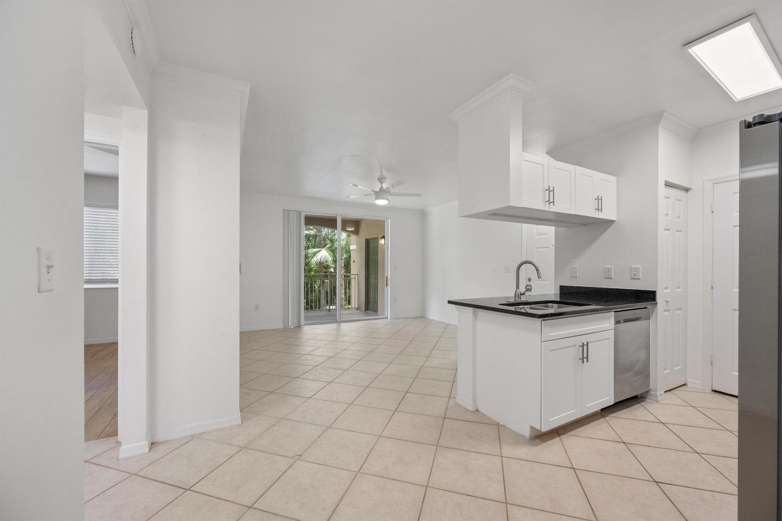 A kitchen with white cabinets and black countertops opens to a tiled living area — 6475 Emerald Dunes Drive # 206, West Palm Beach FL 33411, WEST PALM BEACH, FL