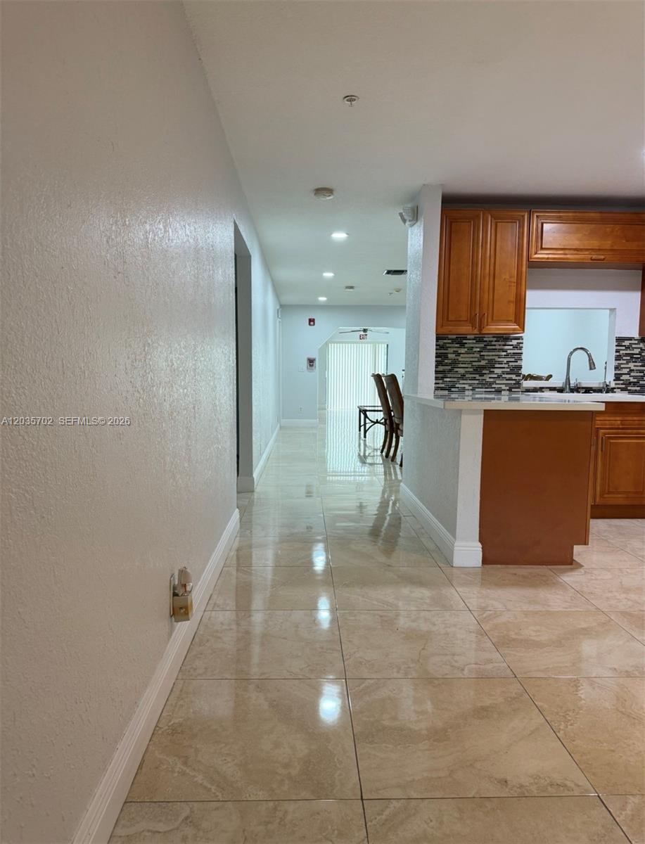 A tiled hallway leads past a kitchen with wood cabinets toward a dining area — CORAL SPRINGS, FL