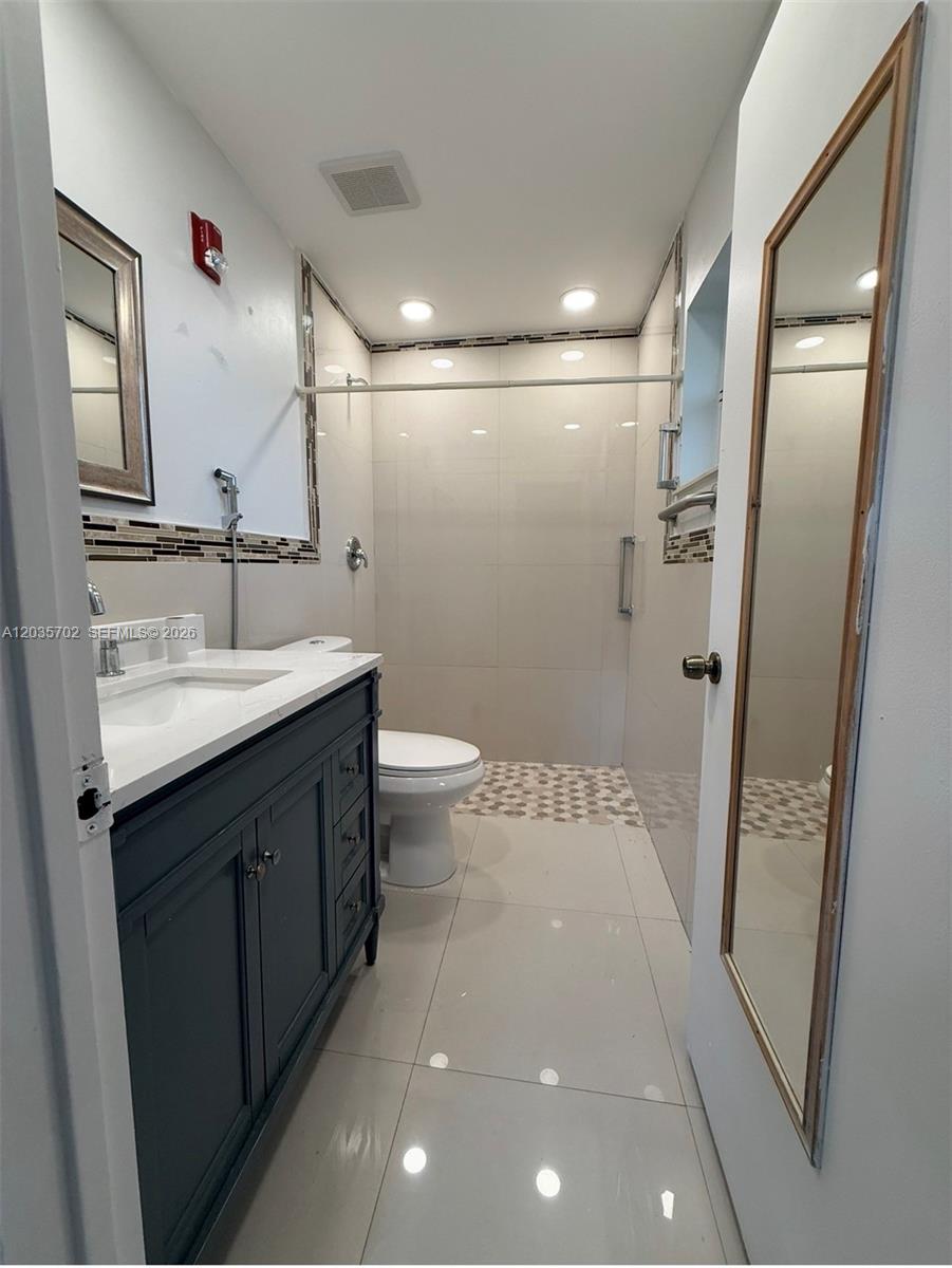 A bathroom features a dark vanity, a walk-in shower with tiled walls, and light flooring — CORAL SPRINGS, FL