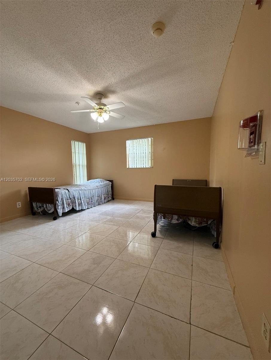 A bedroom with beige walls, tile flooring, a ceiling fan, and two hospital-style beds — CORAL SPRINGS, FL