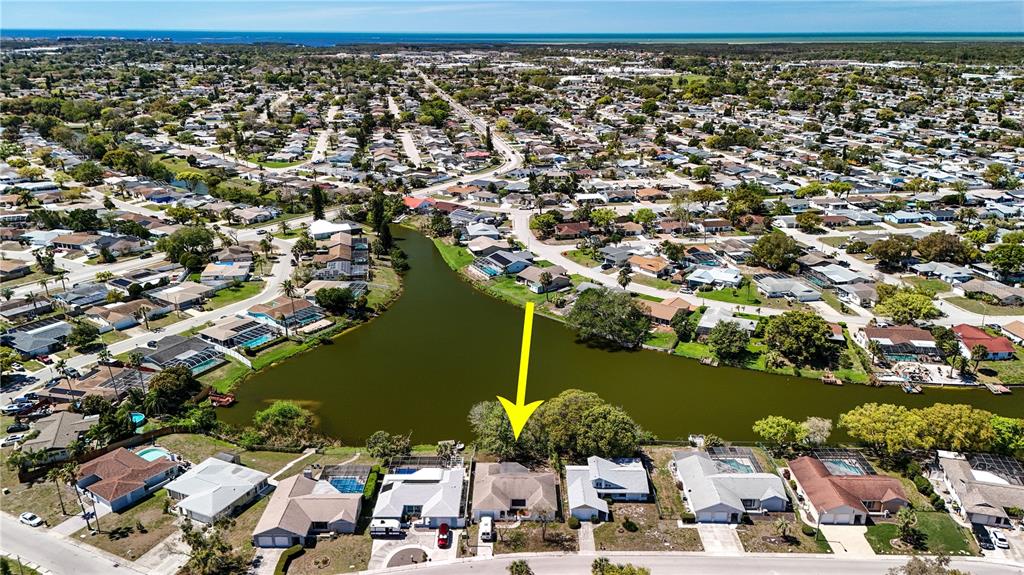 An aerial view shows a residential neighborhood with houses bordering a central lake — 7619 VIENNA LANE, PORT RICHEY, FL