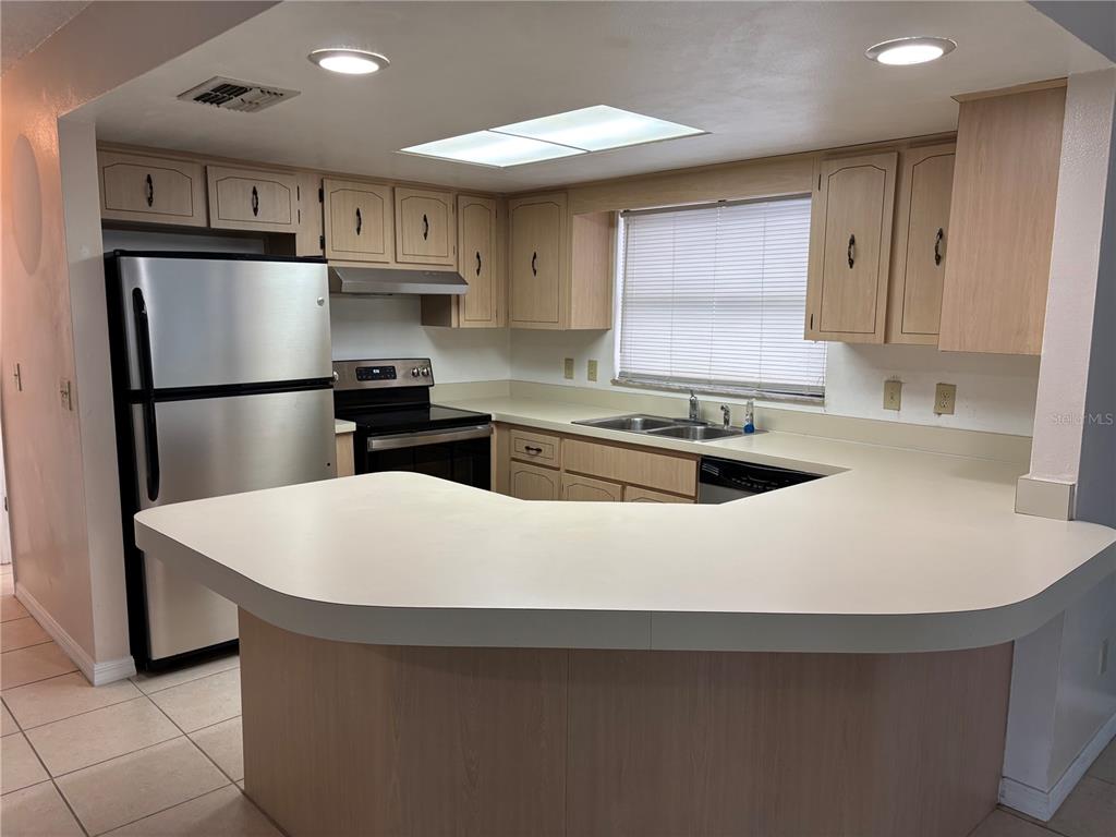 A kitchen features light wood cabinets, stainless steel appliances, and a U-shaped laminate countertop — 7619 VIENNA LANE, PORT RICHEY, FL